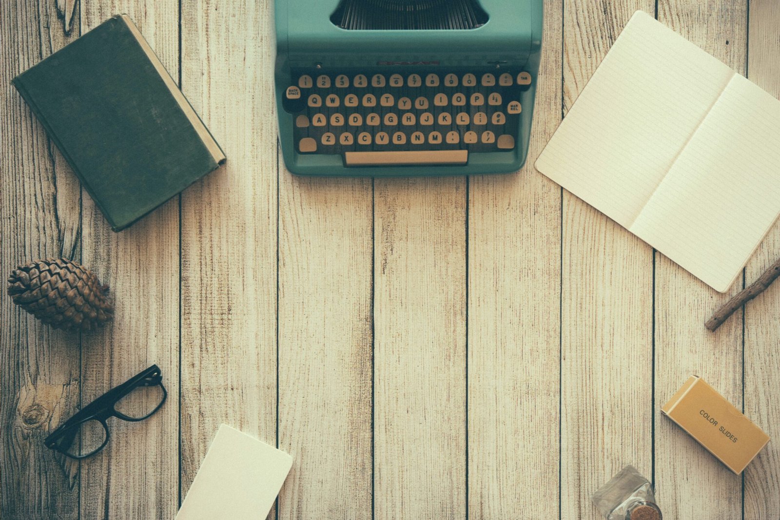 Header image that depicts a wooden writing desk with a book, old fashioned typewriter and other writing materials.